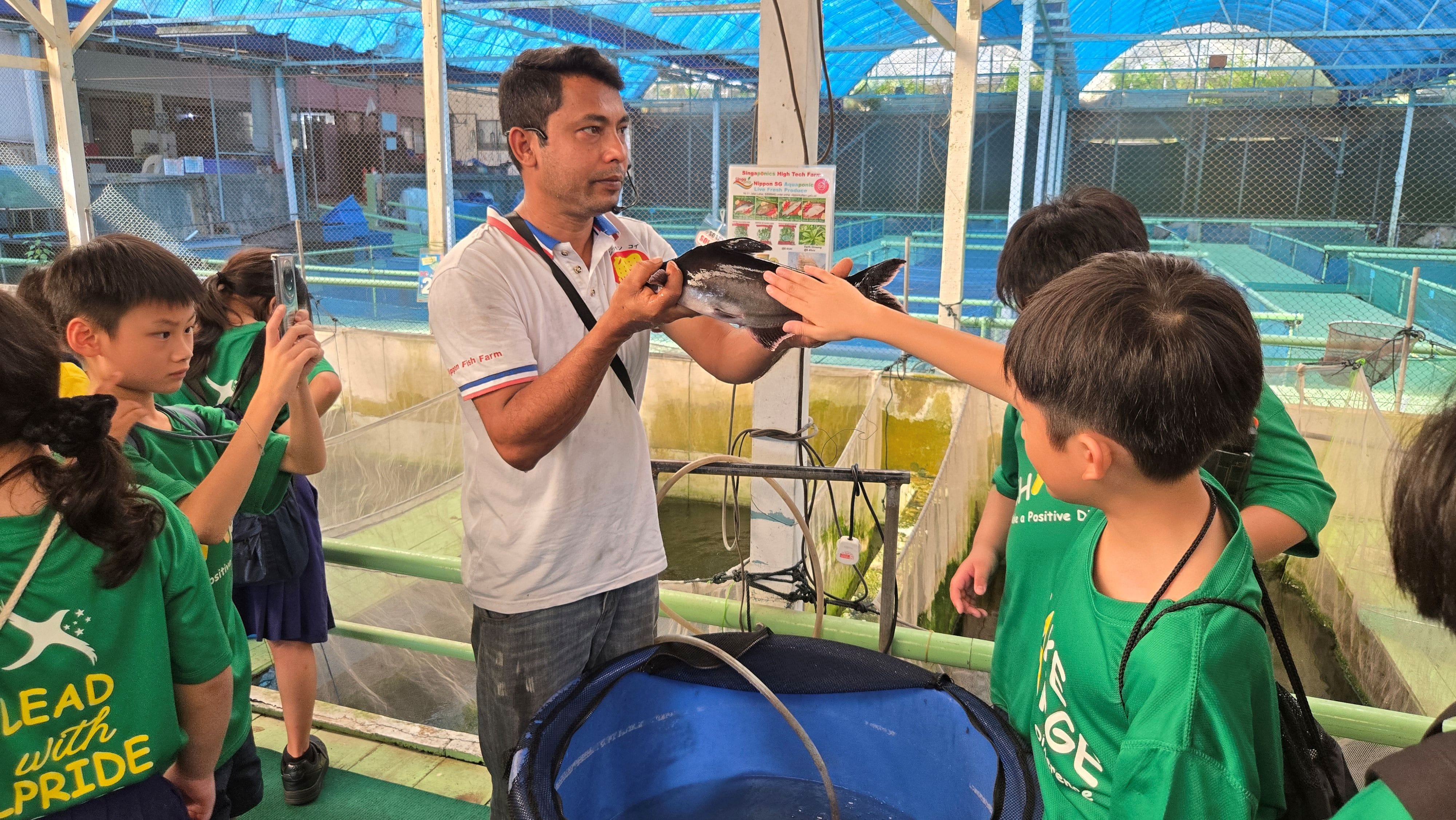 A facilitator holds up a fish as the students are gathered around him to examine the fish up close